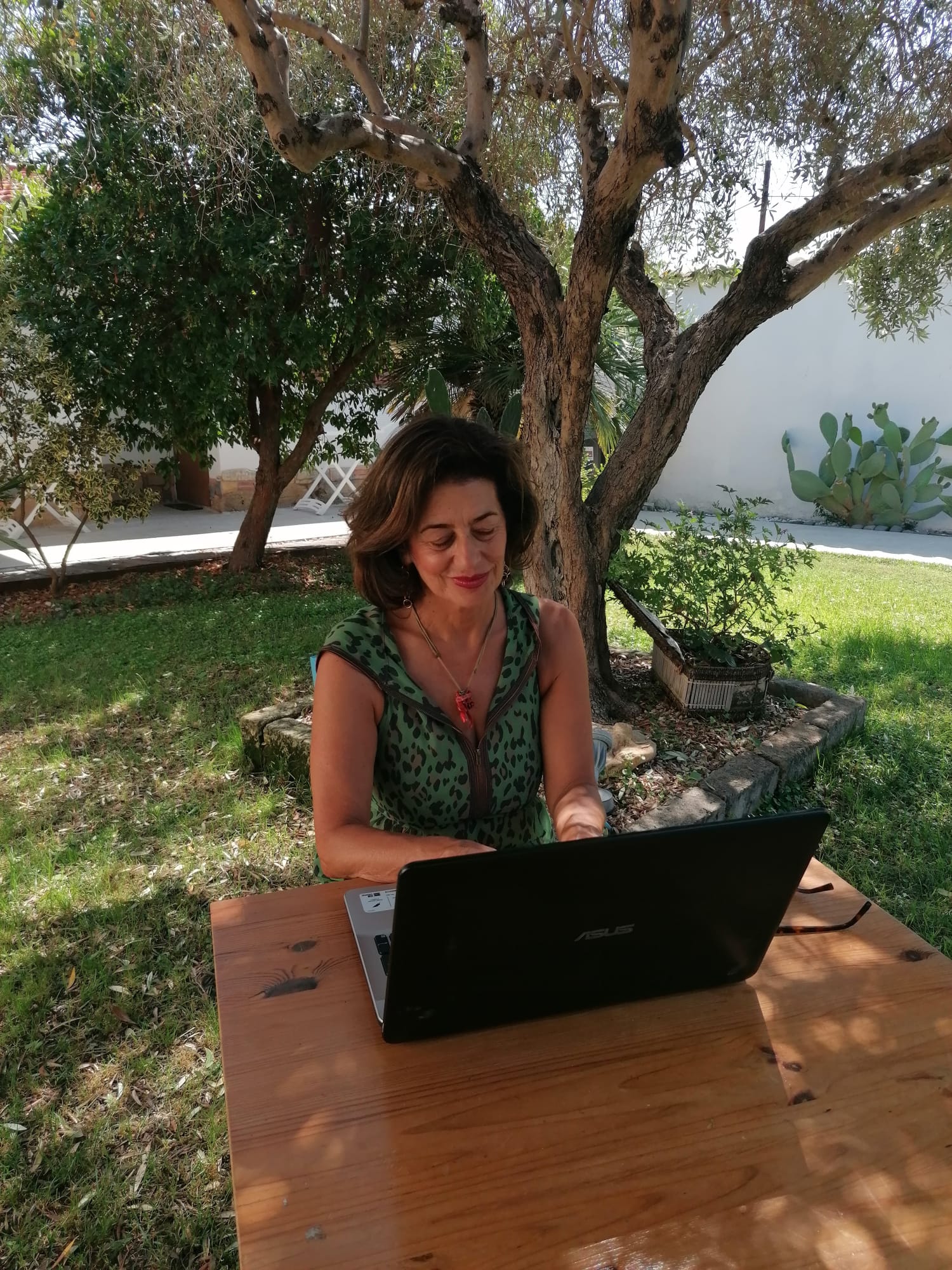 Maria Elena lavora al computer portatile a un tavolo di legno in giardino